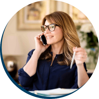 Woman on phone in office setting, smiling and holding a pen, representing personal consultation for tailored insurance solutions at ACS Financial.
