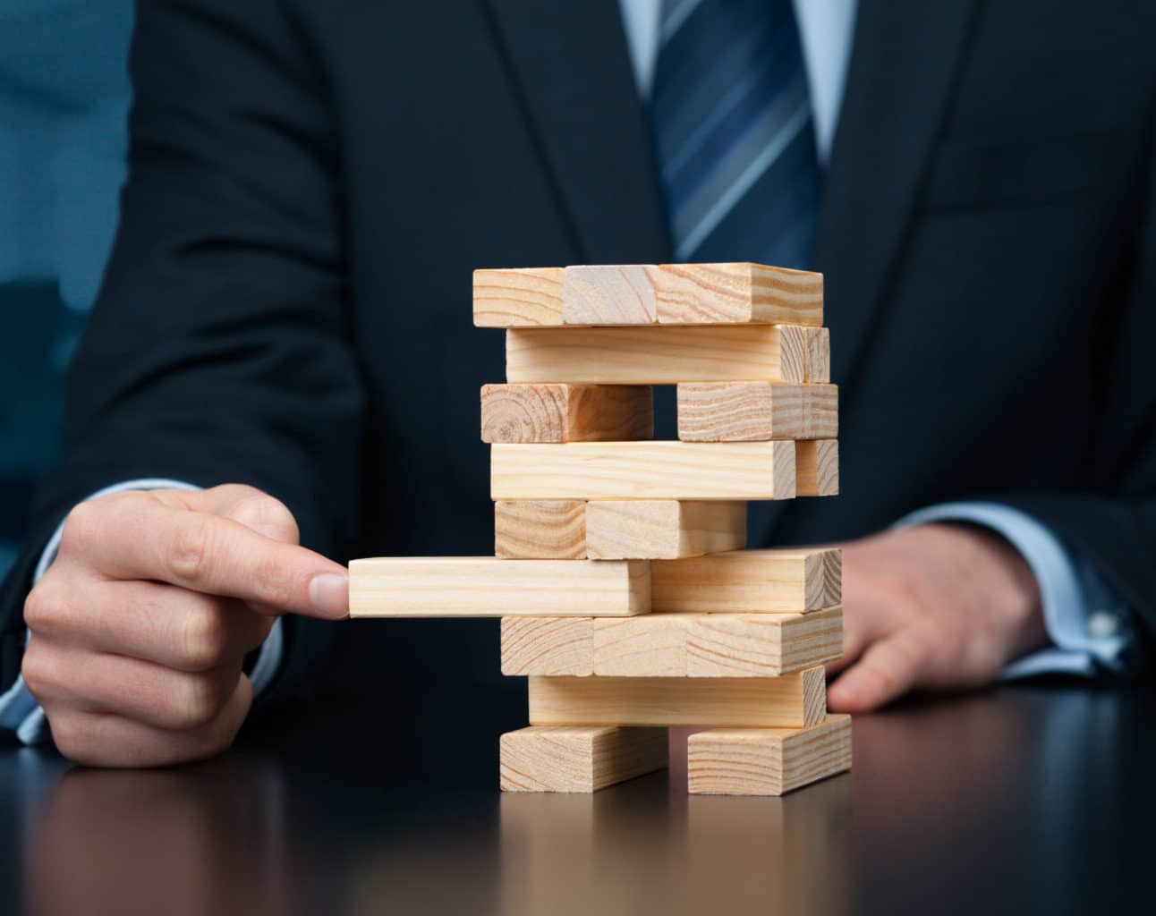 Business professional carefully removing a wooden block from a Jenga-like tower, symbolising risk management and strategic decision-making in commercial insurance.
