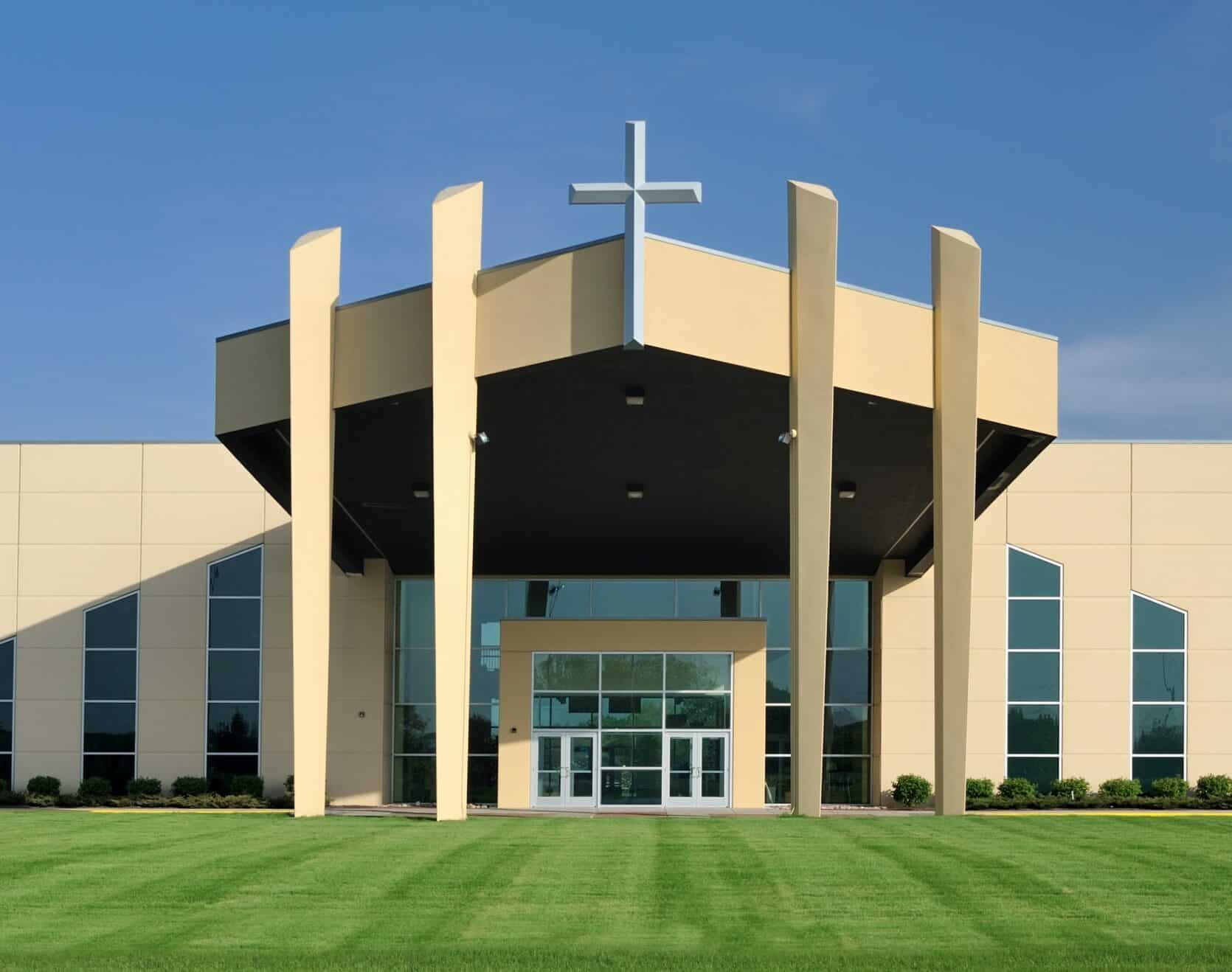 Modern church building facade with prominent cross, large glass windows, and landscaped green lawn, representing Vineyard Christian Church supported by ACS Financial in their growth and facility development.