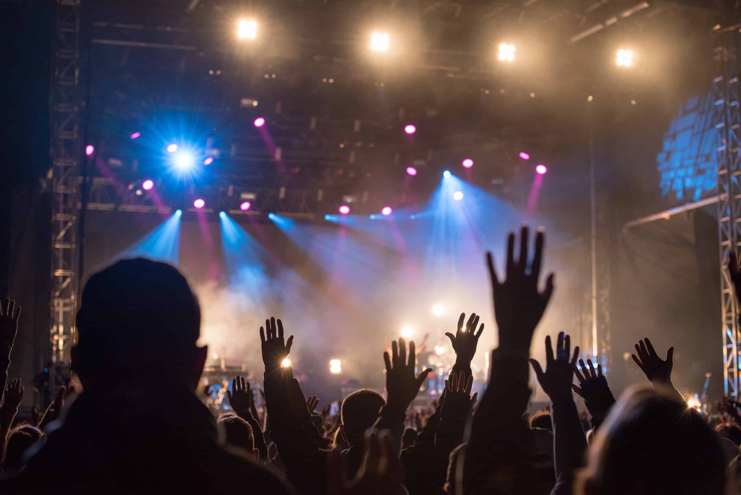 Christians,Raising,Their,Hands,In,Praise,And,Worship,At,A Crowd with raised hands at a vibrant concert, illuminated by colourful stage lights, symbolizing community and worship.