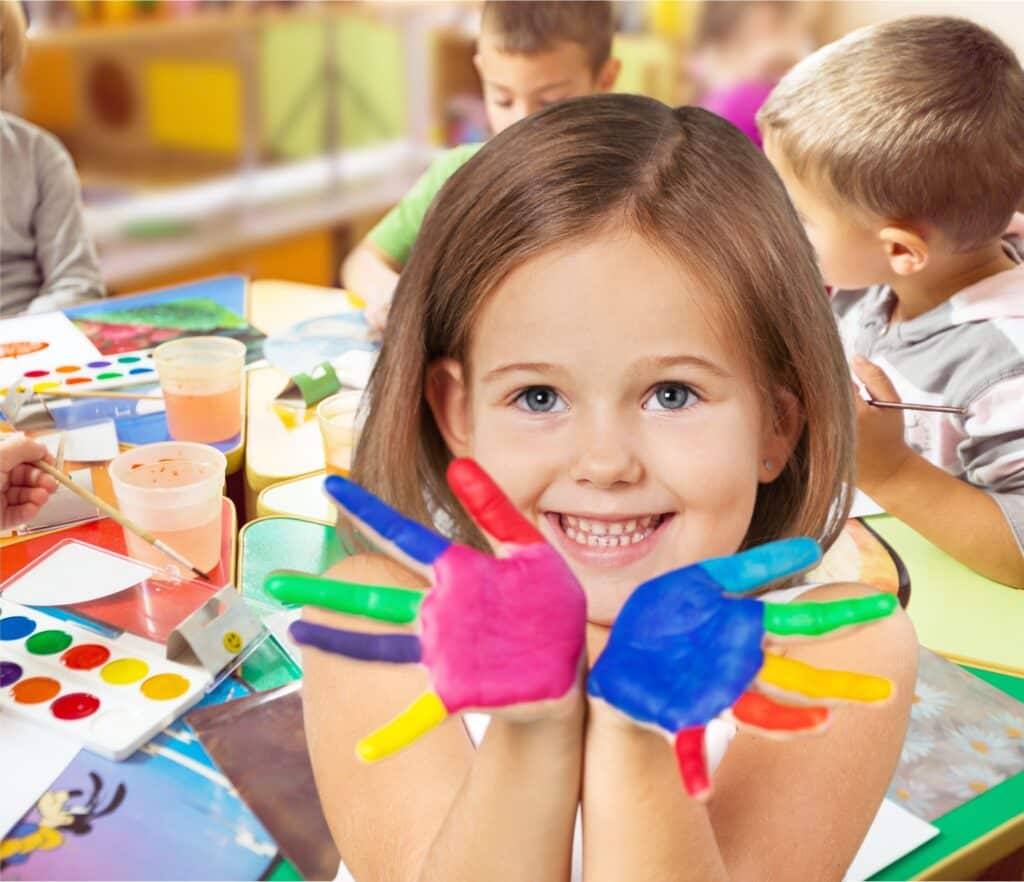 Classroom. Smiling girl showing colourful handprints, engaged in creative activities with classmates in a vibrant classroom setting, highlighting the importance of artistic expression in Christian schools.