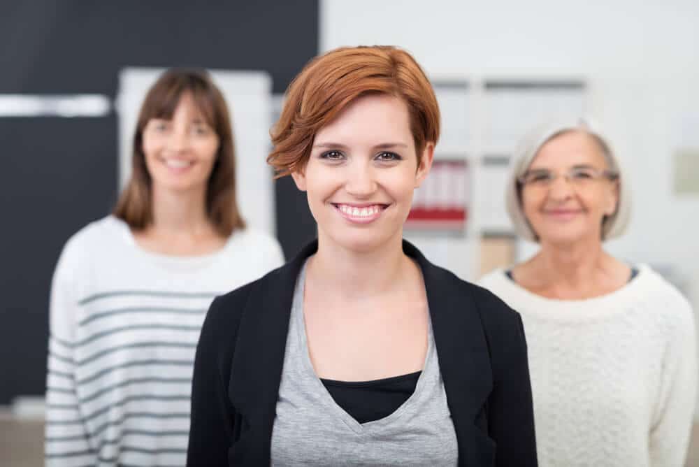 Professional Indemnity types of cover Three women smiling in an office setting, representing a supportive environment for aged care providers, highlighting professionalism and trust in care.