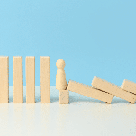 Support worker financial stability Wooden figurine standing on a block, surrounded by upright wooden blocks and a toppled block structure, symbolising stability and support in aged care insurance.
