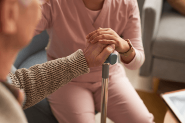 PA Aged care worker assisting elderly person, hands clasped, highlighting personal connection and support in caregiving.