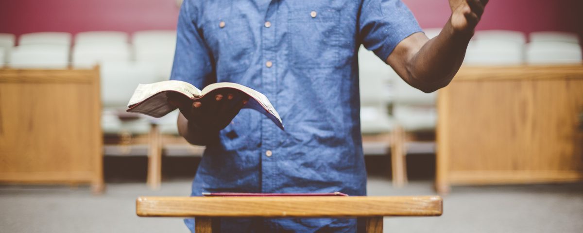 Pastor standing at a pulpit holding an open Bible, illustrating professional indemnity insurance rules for ministers.