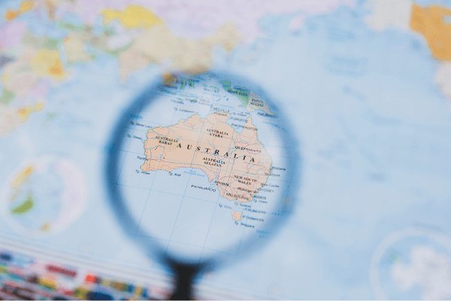 Magnifying glass focusing on a map of Australia, representing national church insurance coverage options.