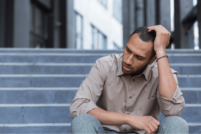 Stressed man sitting on concrete steps, representing personal loss and professional indemnity risks for pastors.