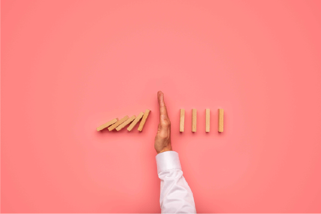 Hand stopping falling domino blocks, representing proactive risk management and management liability for churches.