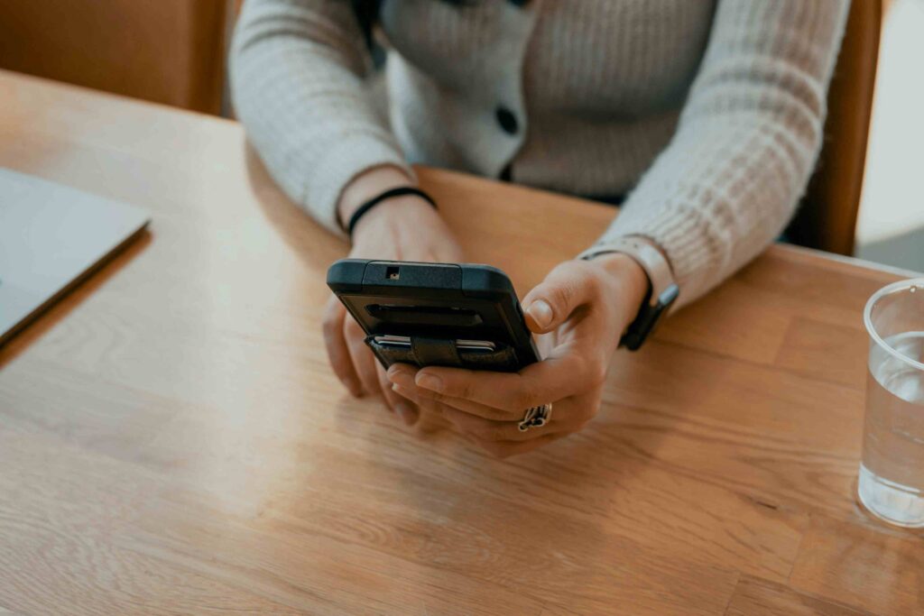 Close-up of a woman using a smartphone at a wooden desk, representing digital church communication and online giving.