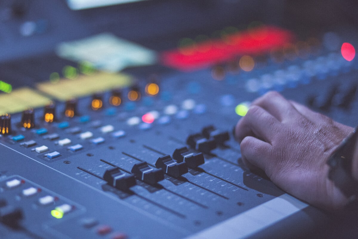 Hand adjusting controls on an audio sound mixer panel console, representing public liability for church stage events.