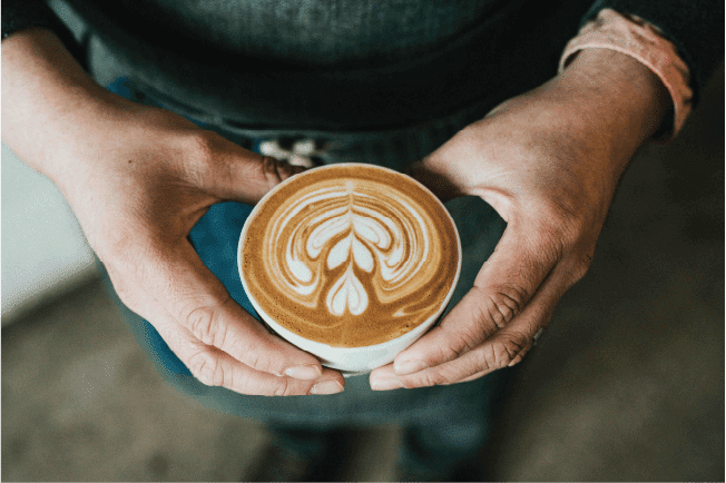 Barista holding a cup of fresh coffee with latte art, representing church cafe operations and public liability.