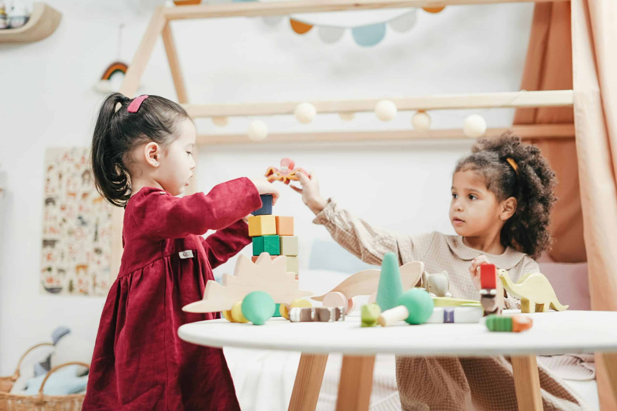 Two children playing with colourful building blocks and wooden toys in a bright and playful childcare environment.