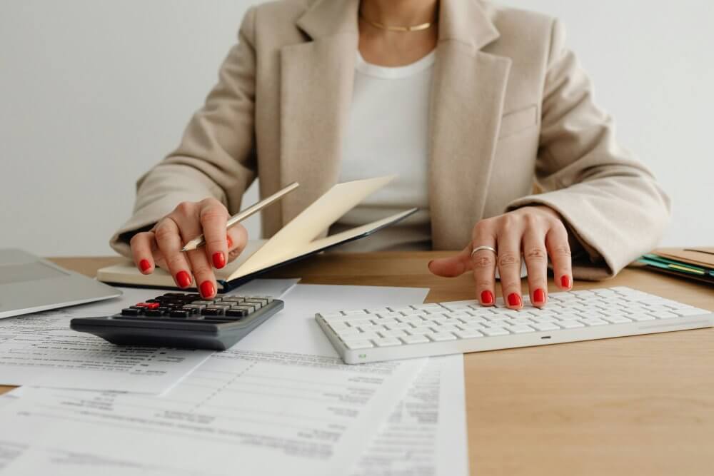 Accountant using a calculator and keyboard to audit financial records, exploring non-profit insurance costs.