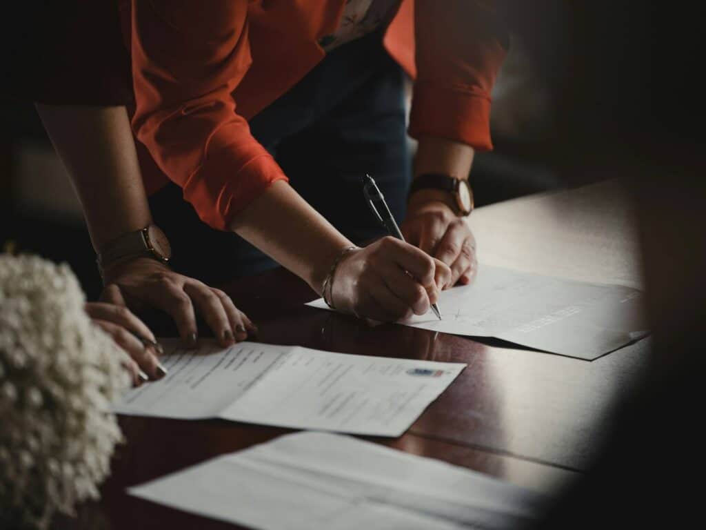 Close-up of hands signing official documentation at a table, managing pricing options for aged care insurance policies.