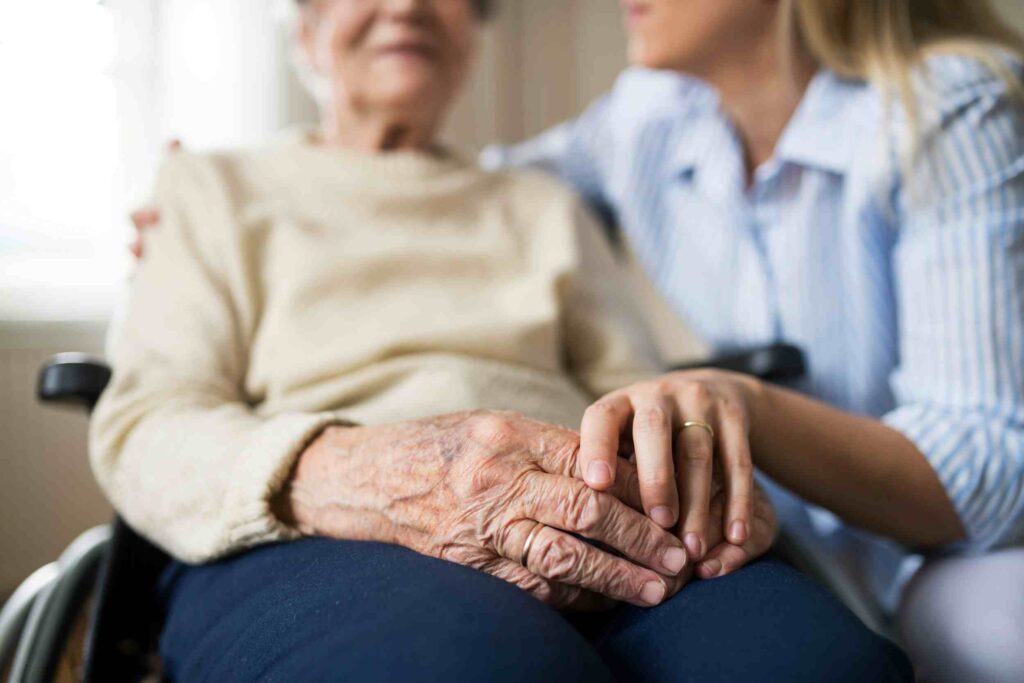Caregiver holding hands with an elderly woman in a wheelchair, illustrating risks faced without aged care insurance.