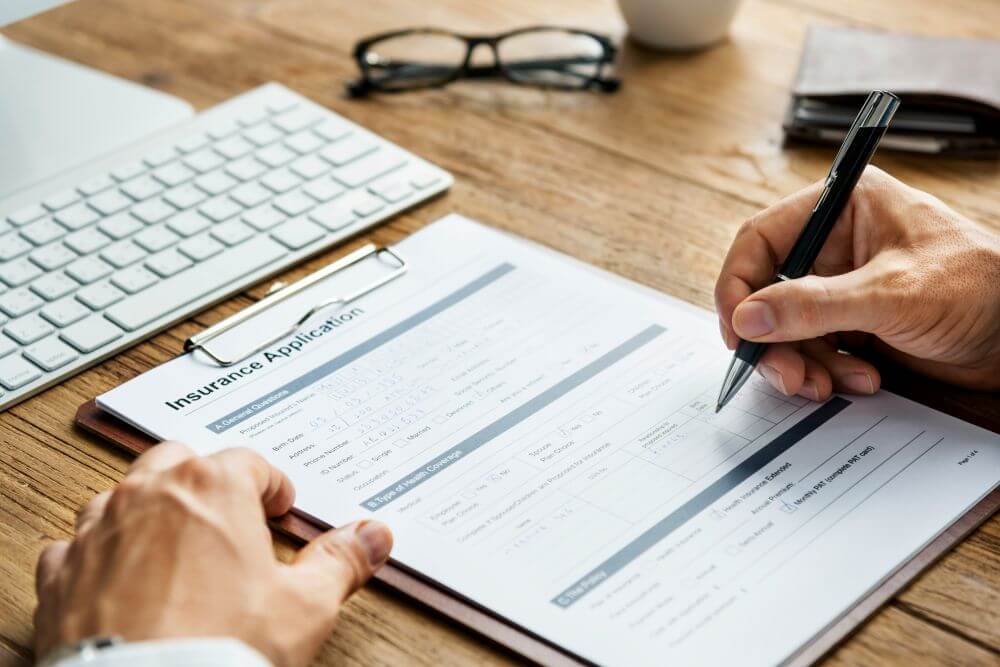 Close-up of hands signing an insurance form at a desk to avoid significant underinsurance risks for a ministry.
