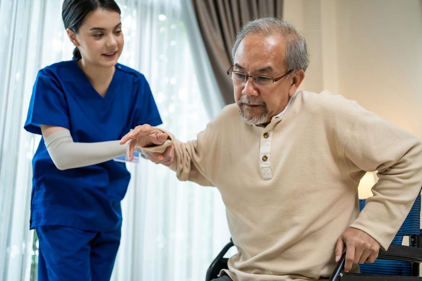 Nurse assisting an elderly gentleman to stand from a wheelchair, highlighting typical risks for aged care insurance.